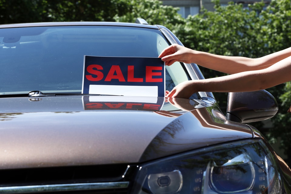 black car with red for sale sign being placed by two hands